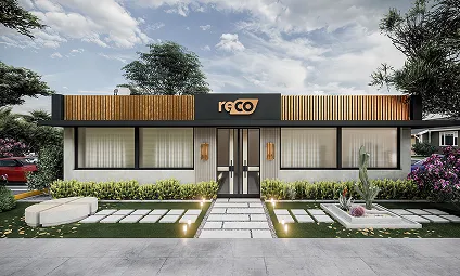 Modern single-story commercial building with large front windows, a central door, and a sign reading 'reco' above the entrance, surrounded by landscaped greenery and a paved pathway.